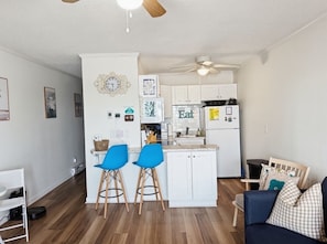 A compact kitchen with white cabinets, a central island, and two blue bar stools.