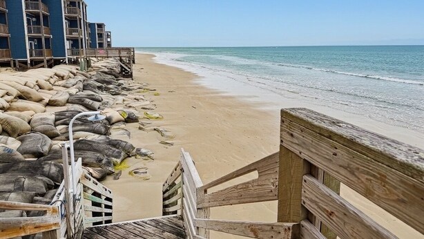 Une plage avec une promenade en bois qui mène à un bâtiment doté de nombreux balcons.