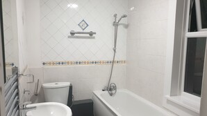 A bathroom with a white bathtub, a sink, and a toilet. There is a showerhead mounted on the wall. - Barnet Luxury Apartment can sleep 4 people just few mins away from Station (Barnet)