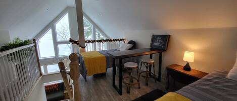 A bedroom with a bed, a desk, two chairs, a lamp, and a window.