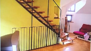 Ein Zimmer mit einer Holztreppe, einem roten Sofa und einem Fenster mit hellem Tageslicht.