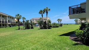 A well-maintained grassy courtyard with palm trees, a clear blue sky, and buildings in the background. - Oceanview 2 bedroom Flat unit 137 (St. Augustine)