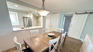 A dining area with a wooden table, white chairs, a chandelier, and a kitchen in the background. - Oceanview 2 bedroom Flat unit 137 (St. Augustine)