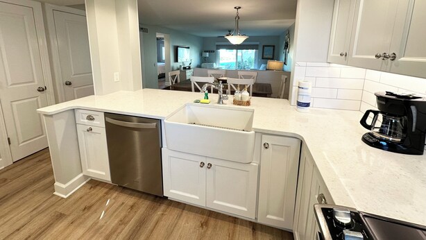 A modern kitchen with white cabinetry, a stainless steel dishwasher, a coffee maker, and a view into the dining area. - Oceanview 2 bedroom Flat unit 137 (St. Augustine)