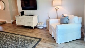 A living room with a white sofa, a white dresser, a flat-screen TV, a lamp, and a patterned rug. - Oceanview 2 bedroom Flat unit 137 (St. Augustine)