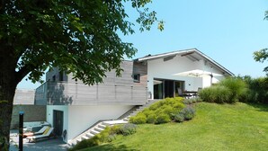 Een modern huis met twee verdiepingen, een overdekt terras, een trap naar de bovenverdieping en een verzorgd gazon.