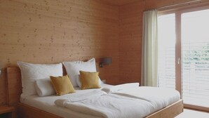 Een slaapkamer met houten lambrisering, een groot bed, nachtkastje en een raam met gordijnen.