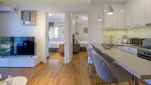 A modern kitchen with white cabinets, a microwave, and a built-in oven. There is a dining area with a bar stool and a TV on a stand. - Lush Sapphire apt. steps from the Acropolis! (Athina)