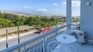A balcony with a white metal table and chairs, overlooking a road with a red double-decker bus. - Lush Sapphire apt. steps from the Acropolis! (Athina)