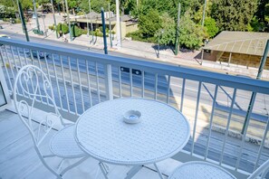 A balcony with a round table and two chairs, overlooking a street with buildings and trees.