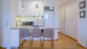 A modern kitchen with white cabinetry, a central island with bar stools, pendant lighting, and a refrigerator. - Lush Sapphire apt. steps from the Acropolis! (Athina)