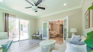 En rummelig stue med ventilator, spiseplads med bord og stole, og udsigt gennem en glasdør til en terrasse.
