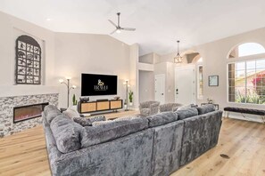 A modern living room with a large sectional sofa, a fireplace, a flat-screen TV, and a ceiling fan. - Tatum Ranch Retreat | Heated Pool & Backyard Fun (Cave Creek)