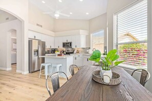 A modern kitchen with white cabinets, stainless steel appliances, and a dining area with a wooden table and chairs.
