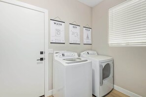 A laundry room with two washing machines, a door, and three wall-mounted signs indicating wash, dry, and fold. - Tatum Ranch Retreat | Heated Pool & Backyard Fun (Cave Creek)