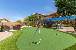 A backyard with artificial turf, a putting green, and outdoor furniture. - Tatum Ranch Retreat | Heated Pool & Backyard Fun (Cave Creek)