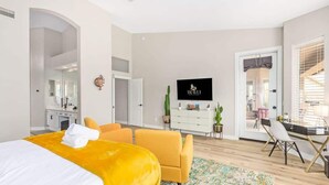 Moderni hotellihuone, jossa on sänky, työpöytä, tuoli, televisio ja ovi, joka johtaa parvekkeelle.