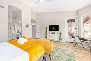 A modern hotel room with a bed, a desk, a chair, a TV, and a door leading to a balcony. - Tatum Ranch Retreat | Heated Pool & Backyard Fun (Cave Creek)