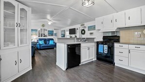 A modern kitchen with white cabinetry, a black dishwasher, and an oven. There is a blue couch in the background. - Near Water: Lake Dallas Home w/ Furnished Patio! (Lake Dallas)