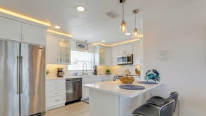 Una cocina moderna con armarios blancos, electrodomésticos de acero inoxidable y una isla central con taburetes de bar.