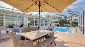 Un espacio al aire libre techado con piscina, mobiliario de mimbre y un paraguas grande.