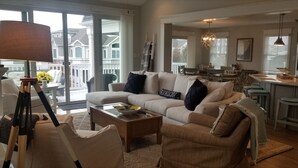 A spacious living room with a large sofa, coffee table, and a dining area with a kitchen in the background. - 159 26th Street - Spacious home in the heart of Avalon, two blocks to beach. (Avalon)