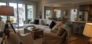 A spacious living room with a large sofa, coffee table, and a dining area with a kitchen in the background. - 159 26th Street - Spacious home in the heart of Avalon, two blocks to beach. (Avalon)