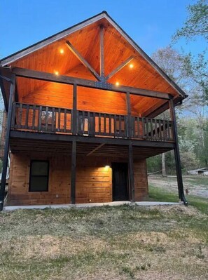 Cozy cabin with a gabled roof and balcony, set amidst a lush lawn and trees.