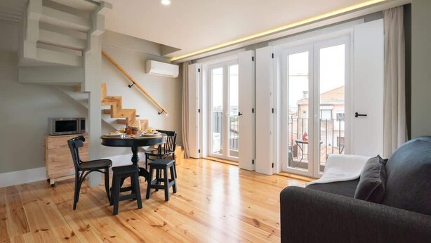 A modern living room with a dining area, wooden flooring, a staircase, and large sliding glass doors leading to an outdoor balcony. - Modern Design Duplex w/ Balcony by HostWise (Porto)