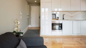 A modern kitchen with white cabinets and a marble backsplash, a gray sofa, and a potted orchid. - Modern Design Duplex w/ Balcony by HostWise (Porto)