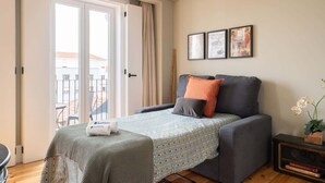 A cozy bedroom with a bed, a small table, and a chair. There is a window with curtains, and a balcony is visible outside. - Modern Design Duplex w/ Balcony by HostWise (Porto)