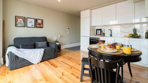 A modern living room with a grey sofa, a dining table with chairs, and a kitchen area with white cabinets. - Modern Design Duplex w/ Balcony by HostWise (Porto)