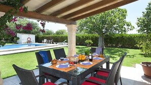 An outdoor patio with a dining table set for four, surrounded by wicker chairs with red cushions. A pool is visible in the background, and the area is covered by a wooden pergola. - Finca Burga, vacation home in a quiet location, views, pool, A/C, Wifi (Puerto Pollenca)
