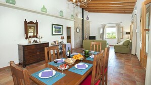 A dining area with a wooden table set for four, surrounded by chairs. There is a wooden cabinet with a mirror and decorative items on the wall. A green sofa is visible in the background. - Finca Burga, vacation home in a quiet location, views, pool, A/C, Wifi (Puerto Pollenca)