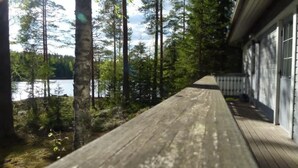 Une terrasse en bois qui mène à un bâtiment d’où l’on peut admirer un lac et des arbres.