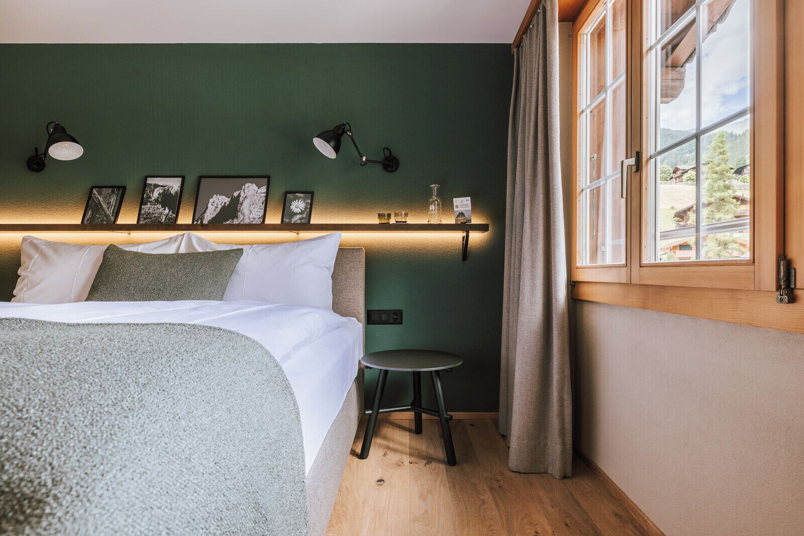 Een slaapkamer met een bed, een klein rond tafeltje, wandlampen en ingelijste foto's.