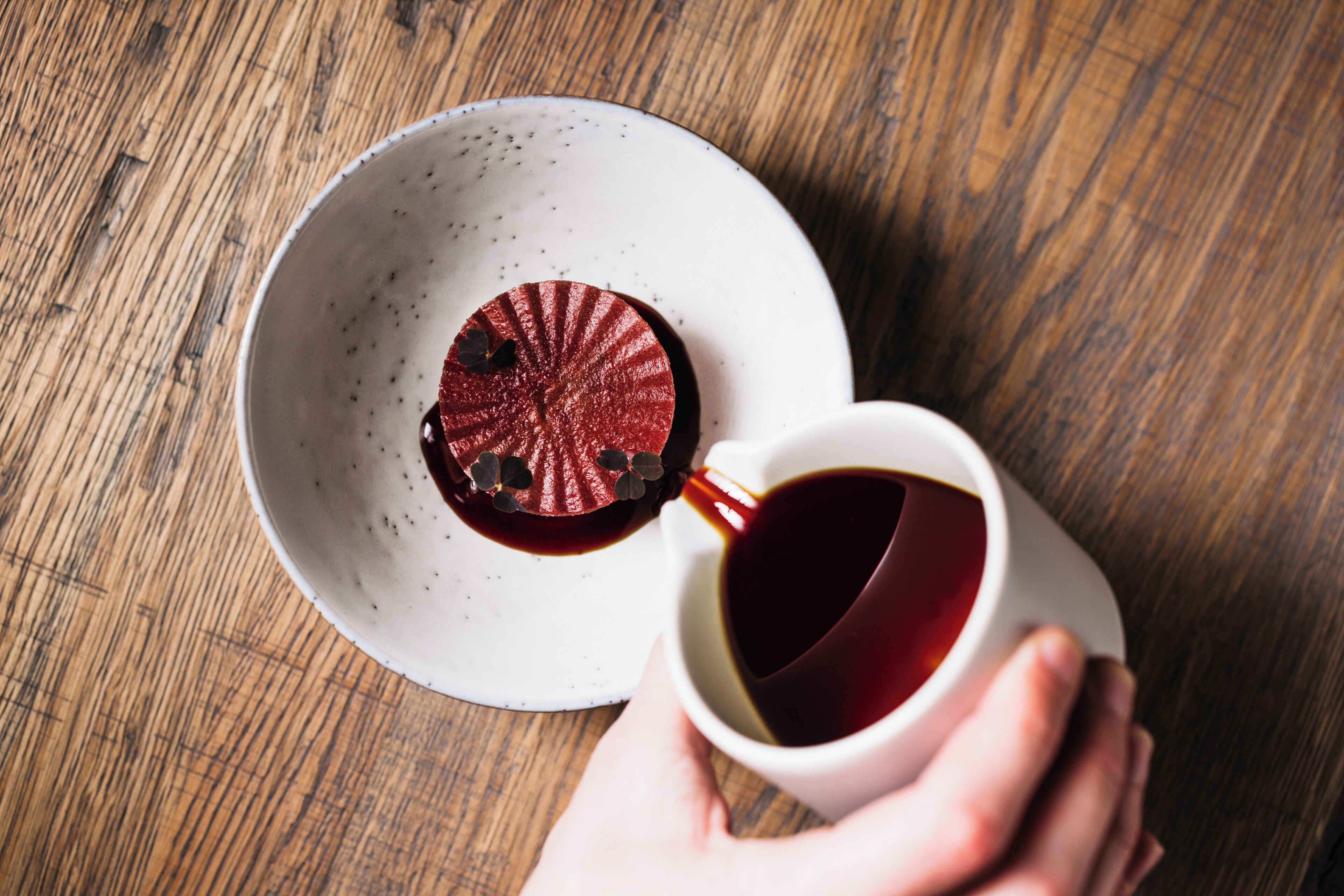 Une main tenant une tasse de café avec une soucoupe sur une table en bois.