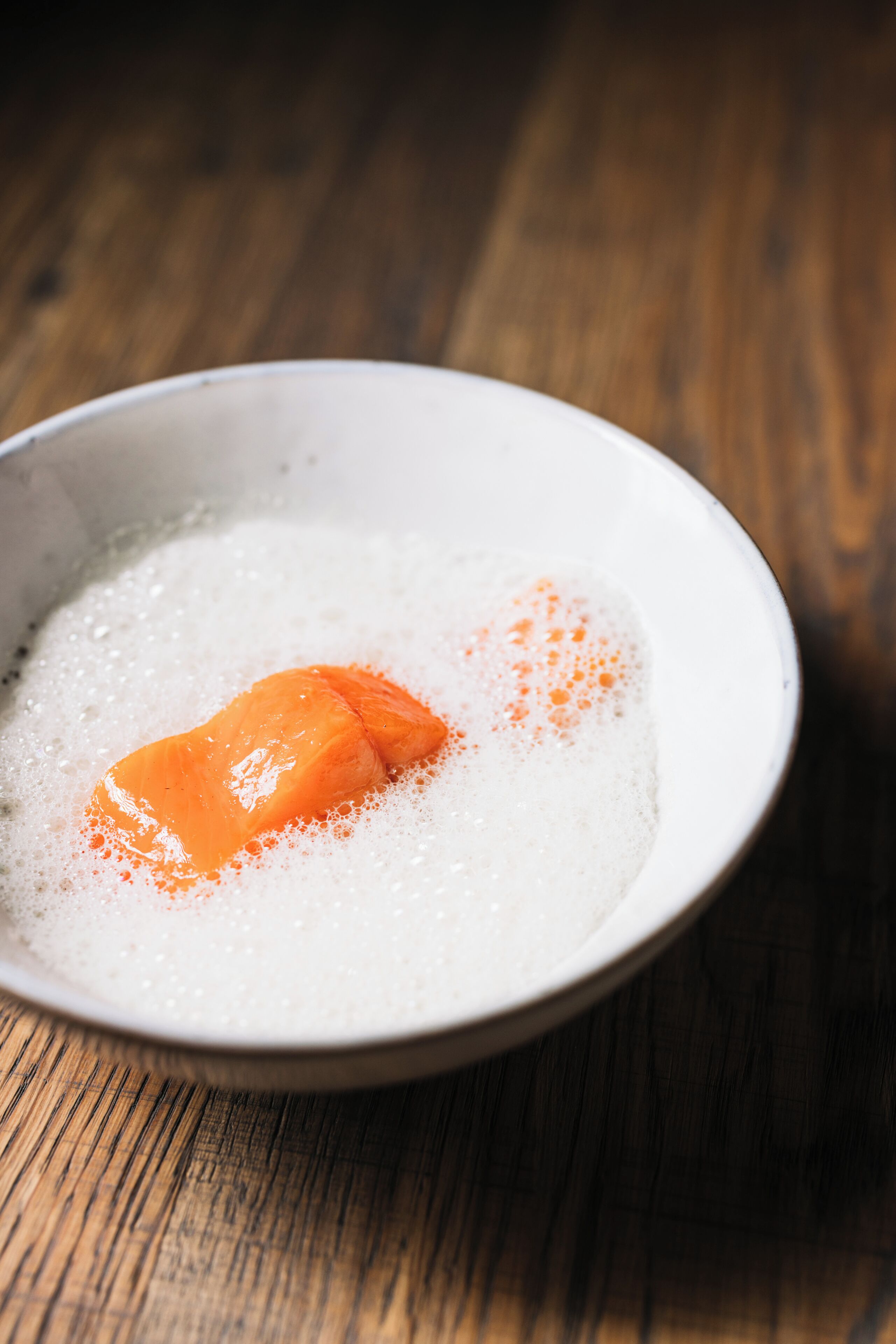 Uma tigela com um pedaço de salmão sobre uma superfície de madeira.