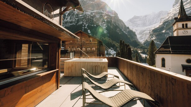 A wooden chalet with a hot tub, lounge chairs, and a mountain view. - Hotel Fiescherblick (Grindelwald)