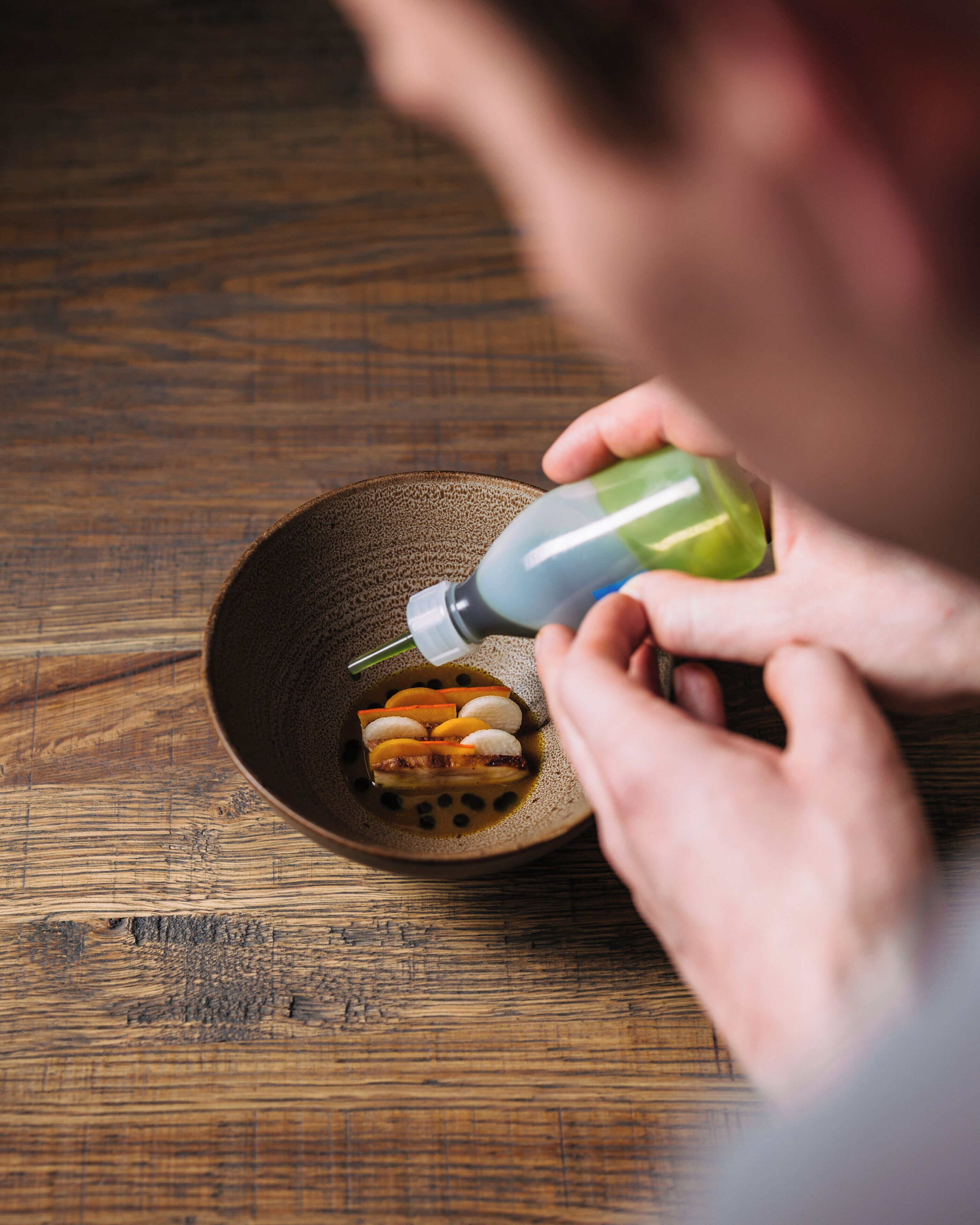 Une personne verse un liquide d’une bouteille dans un bol contenant des aliments.