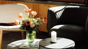 A room with a sofa, a round table with a book and a vase of flowers, and a window with wooden shutters. - Hotel Fiescherblick (Grindelwald)