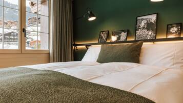 A bed with white linens and a green throw, a bedside lamp, and framed pictures on the wall.