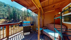 A wooden cabin with a deck, a grill, a bench, and a window overlooking a forested area. - Take it EZ cabin overlooking the river with HOT TUB  on the deck 5 min to Estes! (Drake)