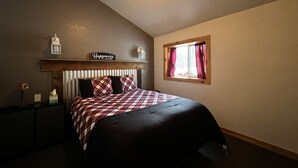 A bedroom with a bed, a nightstand, a lamp, a window with curtains, a ceiling fan, and a sign on the wall. - Take it EZ cabin overlooking the river with HOT TUB  on the deck 5 min to Estes! (Drake)