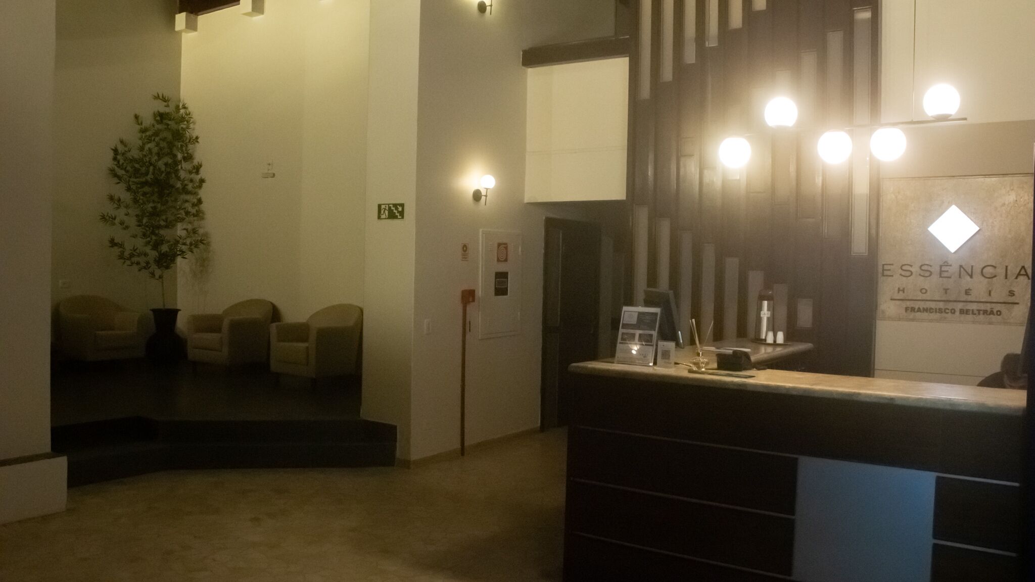 Un espace d’accueil d’hôtel comprenant un comptoir de réception, une plante et un coin salon avec des chaises.