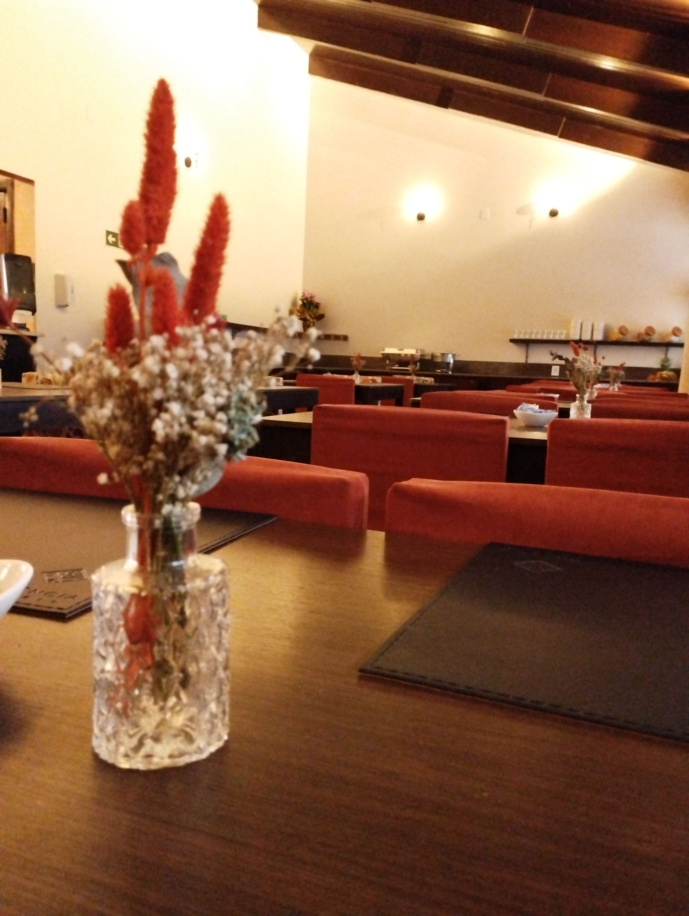 A dining area with red upholstered chairs, a wooden table, and a vase with dried flowers.