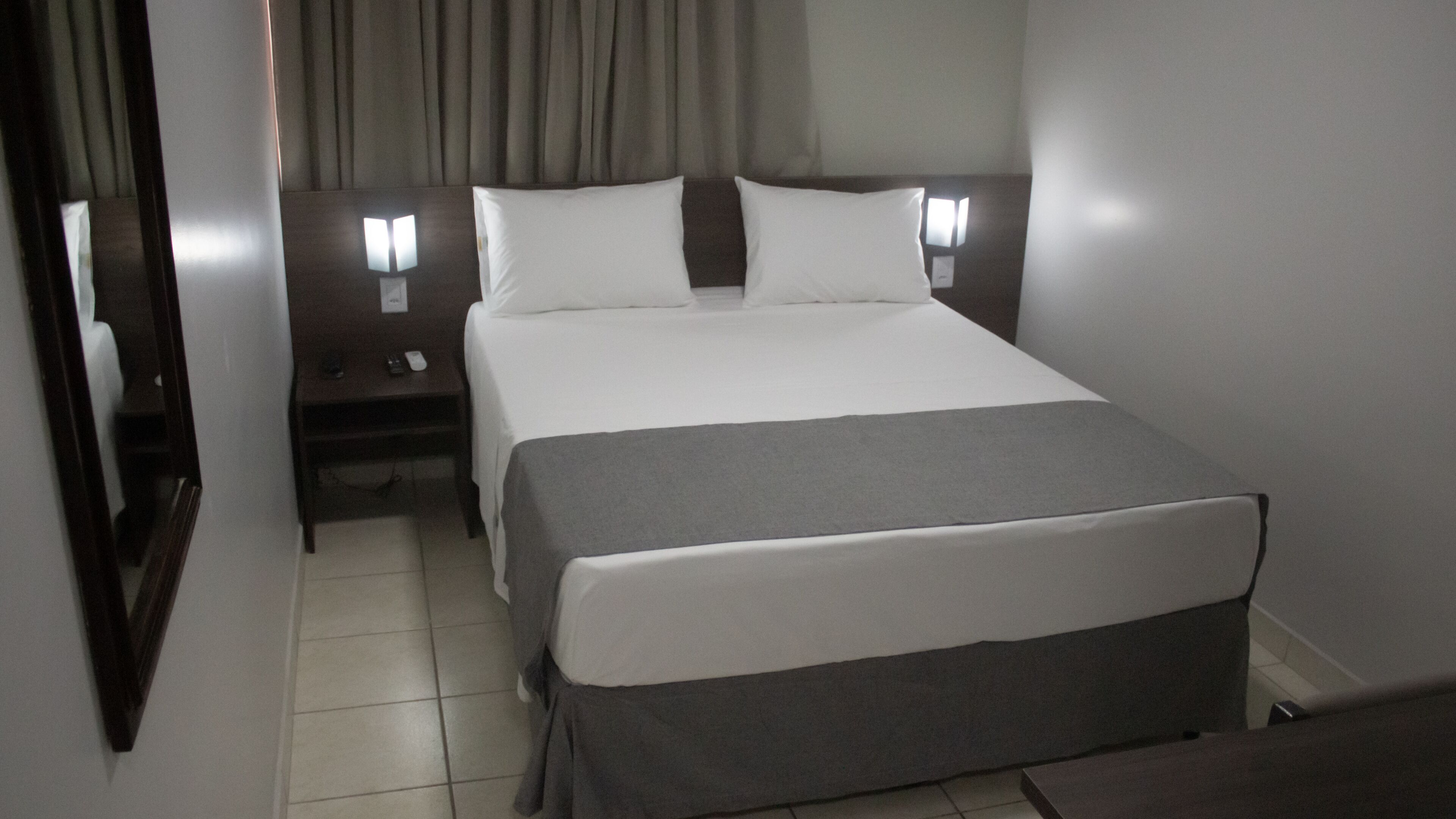 Una habitación de hotel con cama, mesitas de noche, lámpara y espejo.