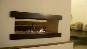 A modern fireplace with a stone base and a dark mantel, set in a neutral-toned room with a minimalist design.