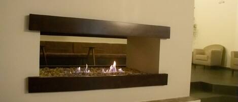 Una chimenea moderna con base de piedra y un fuste oscuro, ubicada en un espacio de tonos neutros con diseño minimalista.
