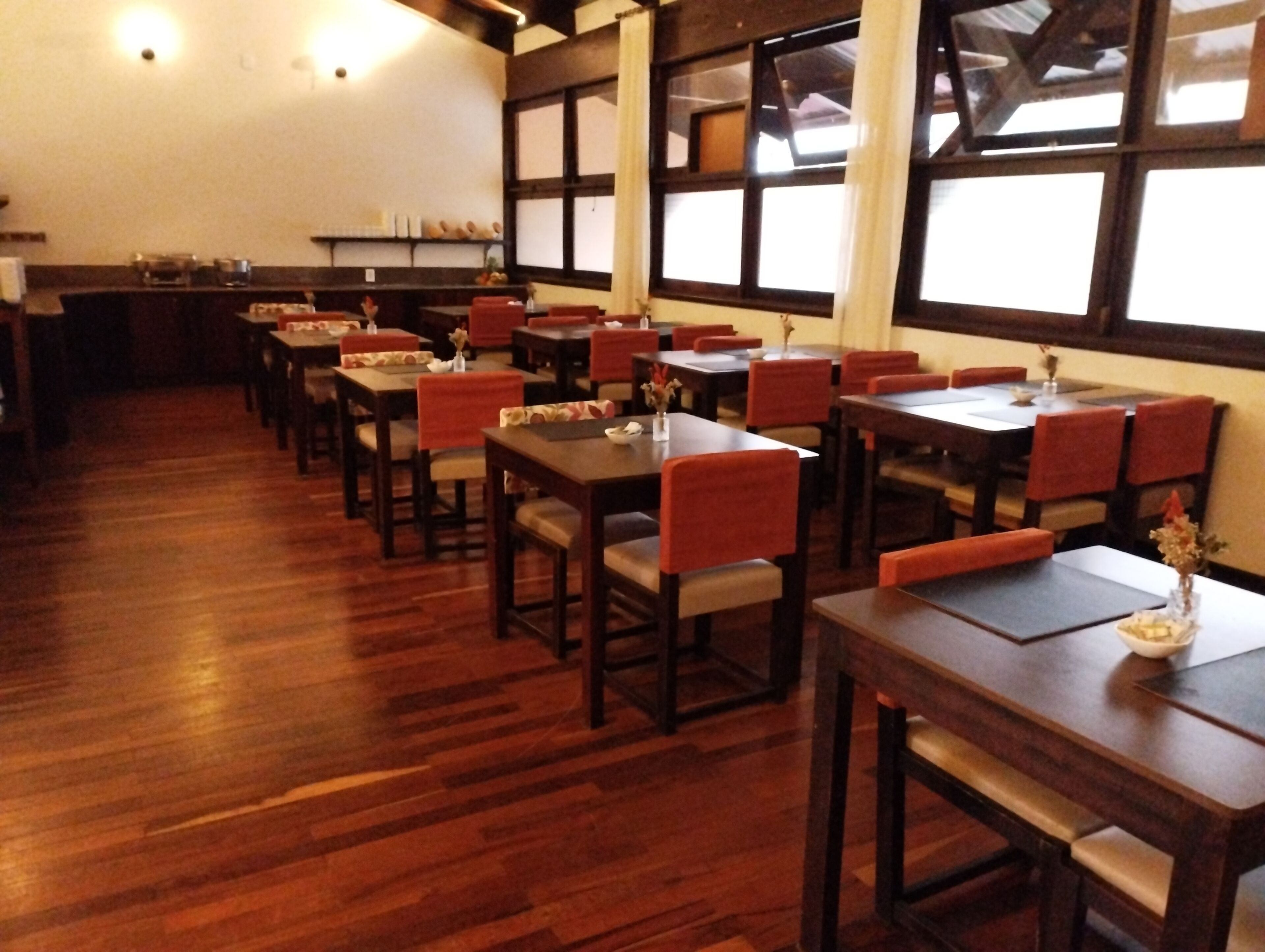 Un restaurante con suelo de madera, sillas tapizadas en rojo y mesas.